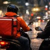 夜の都市でバイクに乗り稼働するフードデリバリー配達員の後ろ姿